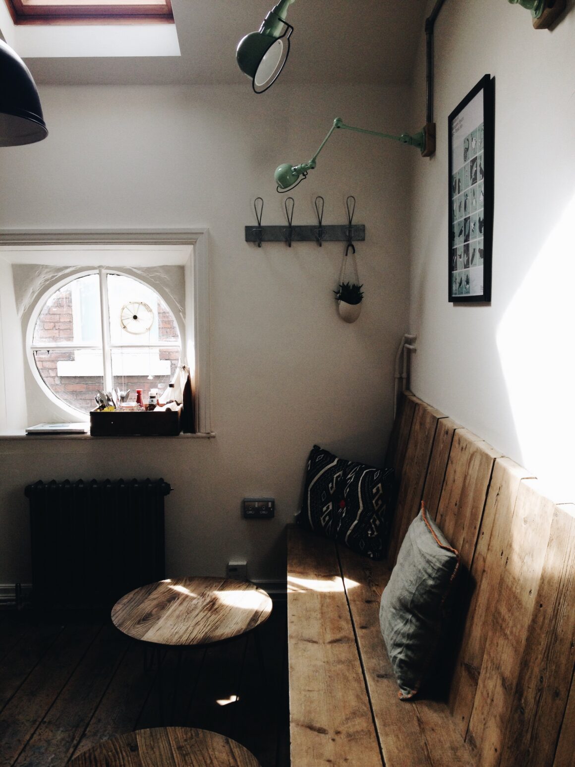A quiet corner with a wooden bench, cushions, and a small round table with a clear top, in a soft window light