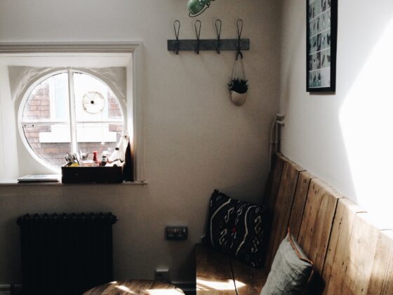 A quiet corner with a wooden bench, cushions, and a small round table with a clear top, in a soft window light