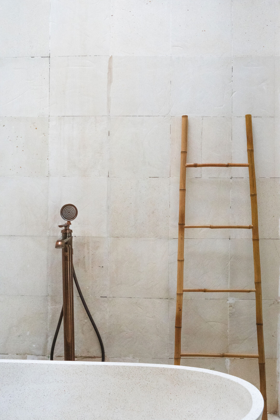 A textured natural stone bathroom wall with an aged brass fixture and wooden ladder, showing well-maintained home materials.