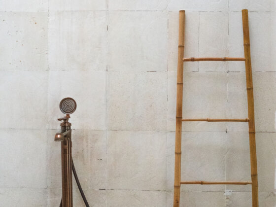 A textured natural stone bathroom wall with an aged brass fixture and wooden ladder, showing well-maintained home materials.