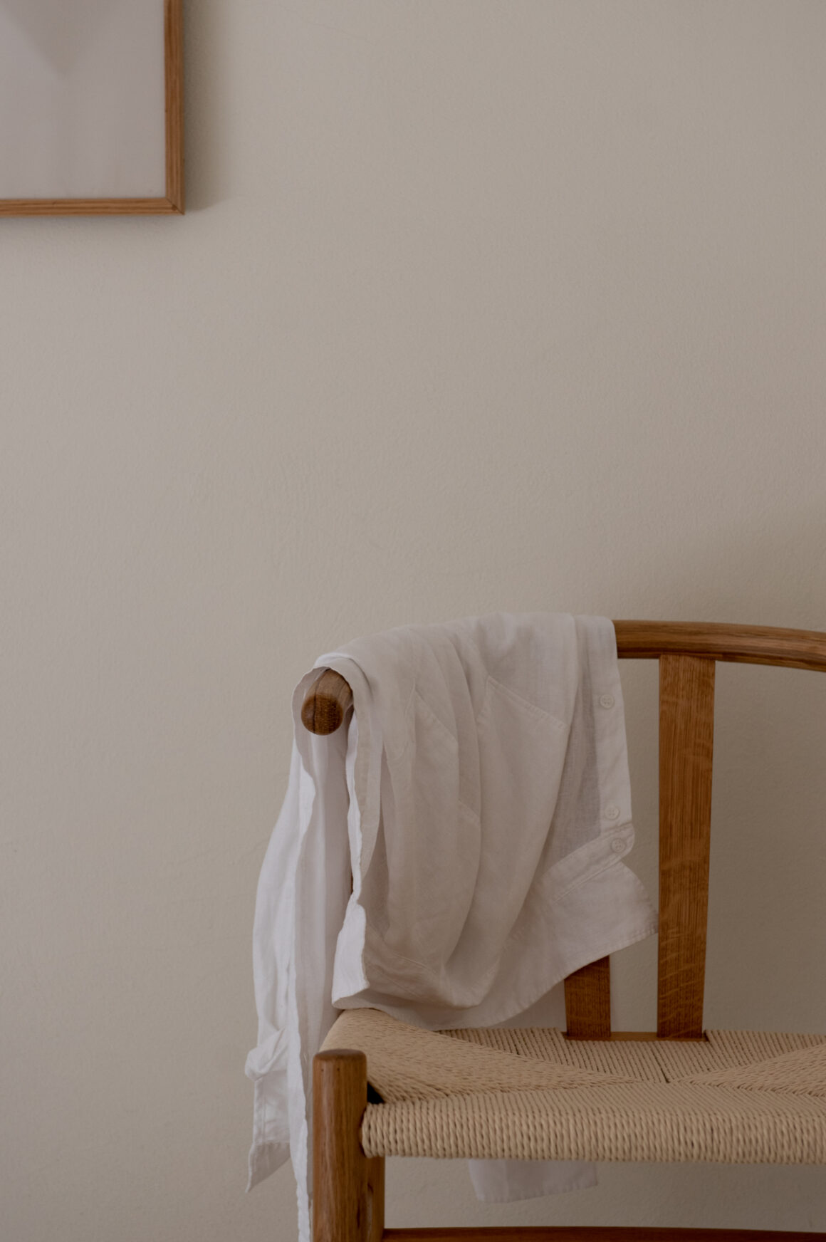 A single piece of white linen draped over a wooden chair against a soft empty wall.