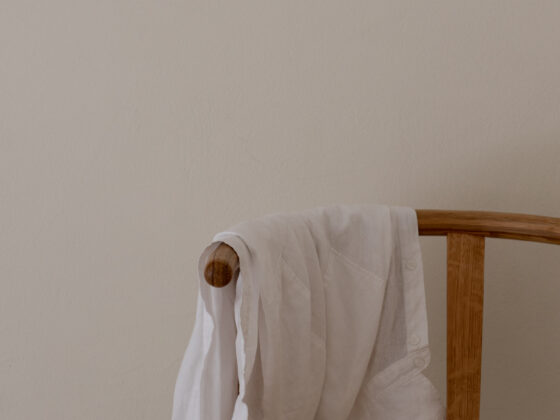 A single piece of white linen draped over a wooden chair against a soft empty wall.