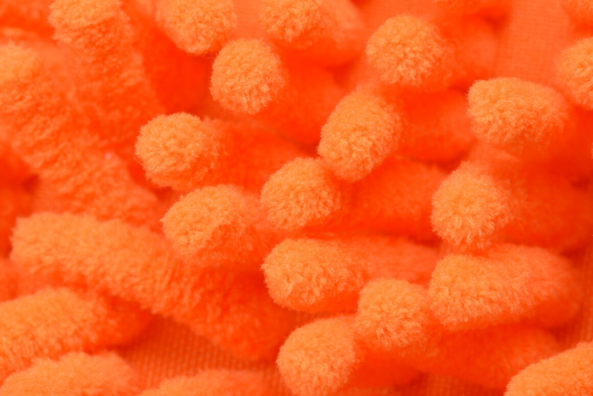 Overhead extreme close-up of orange microfiber cloth filling the frame with dense rounded tufts of synthetic fiber