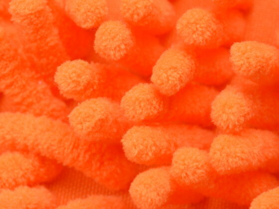 Overhead extreme close-up of orange microfiber cloth filling the frame with dense rounded tufts of synthetic fiber