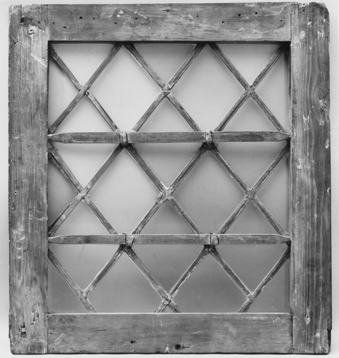 An old diamond-pane leaded window in a weathered wood frame, black and white