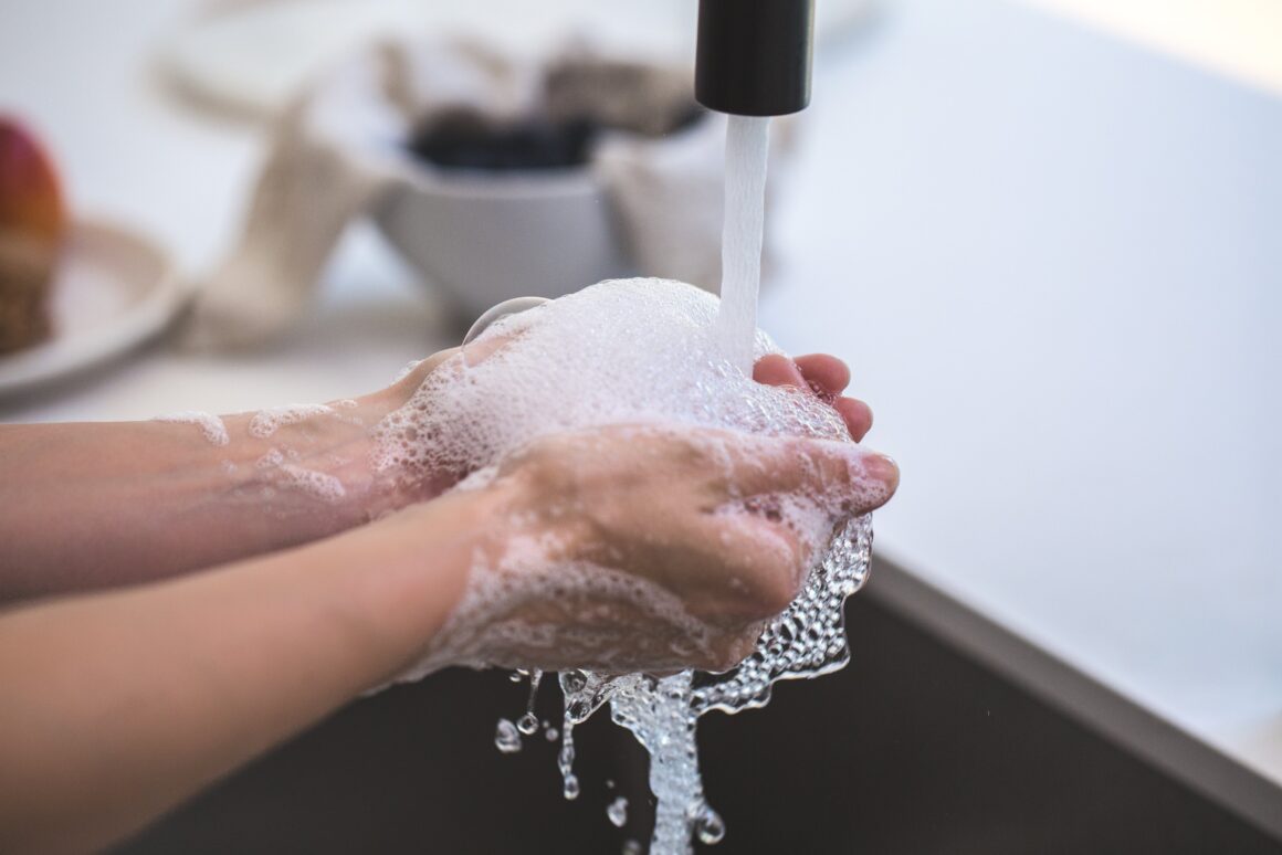 Hands covered in white soapy foam under a stream of running water at a sink