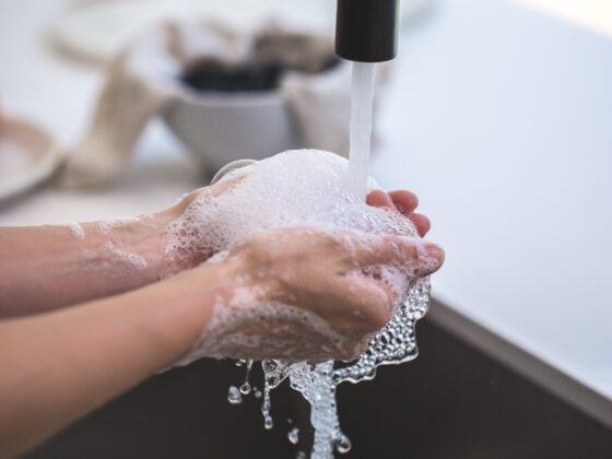 Hands covered in white soapy foam under a stream of running water at a sink