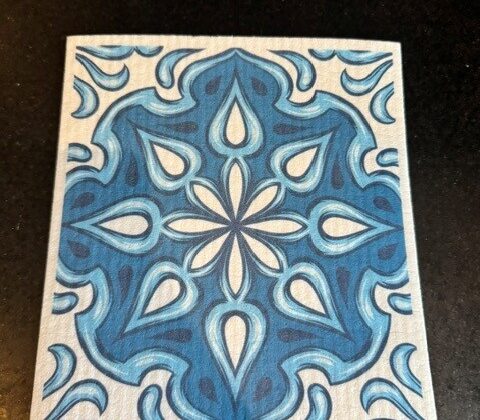 A dry Swedish dishcloth with a blue and white tile pattern resting on a dark counter