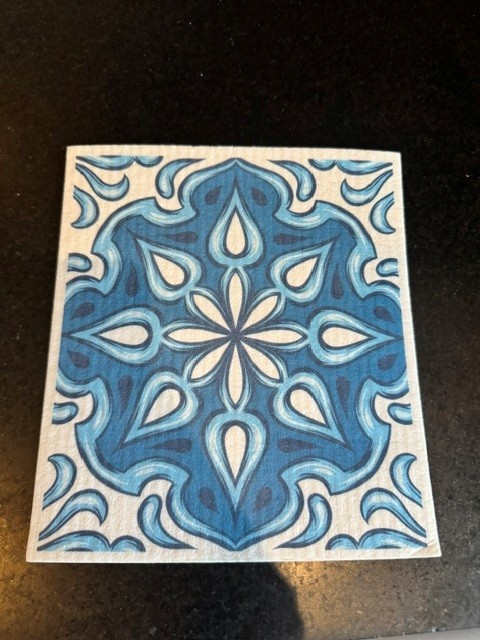 A dry Swedish dishcloth with a blue and white tile pattern resting on a dark counter
