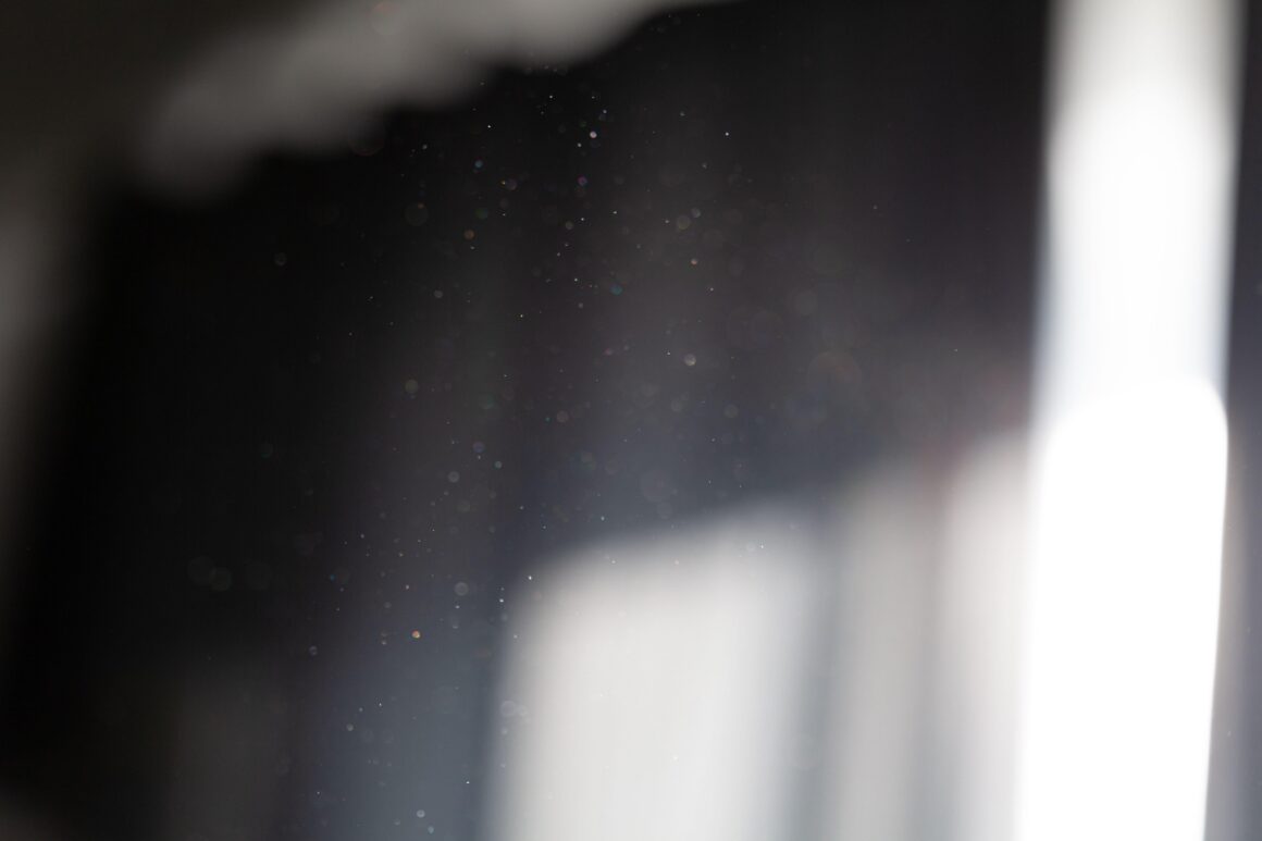 Fine dust particles suspended in a beam of sunlight coming through a window in a dim room.