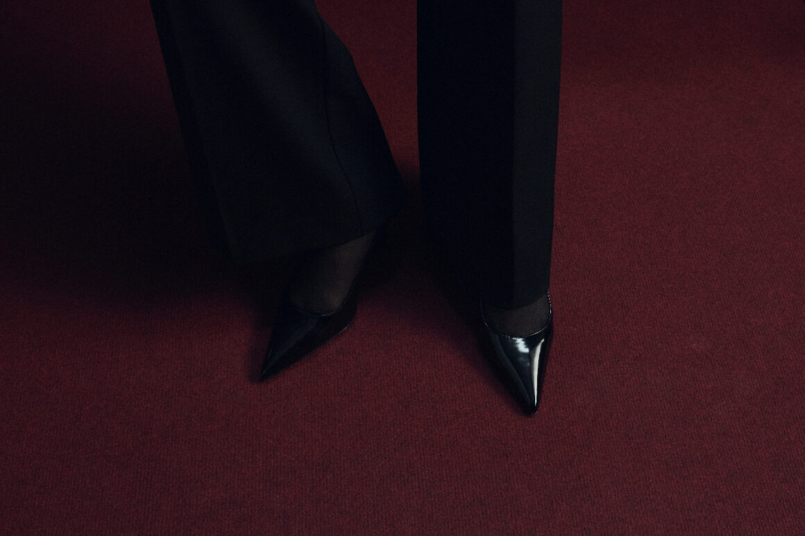 Black pointed shoes standing on a deep red carpet in low light