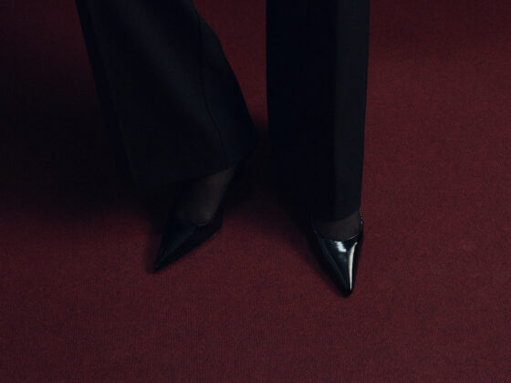 Black pointed shoes standing on a deep red carpet in low light