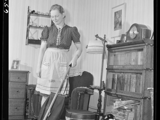 Woman with a vintage upright vacuum cleaner in a wood-paneled living room, the kind that can send dust back into the air.