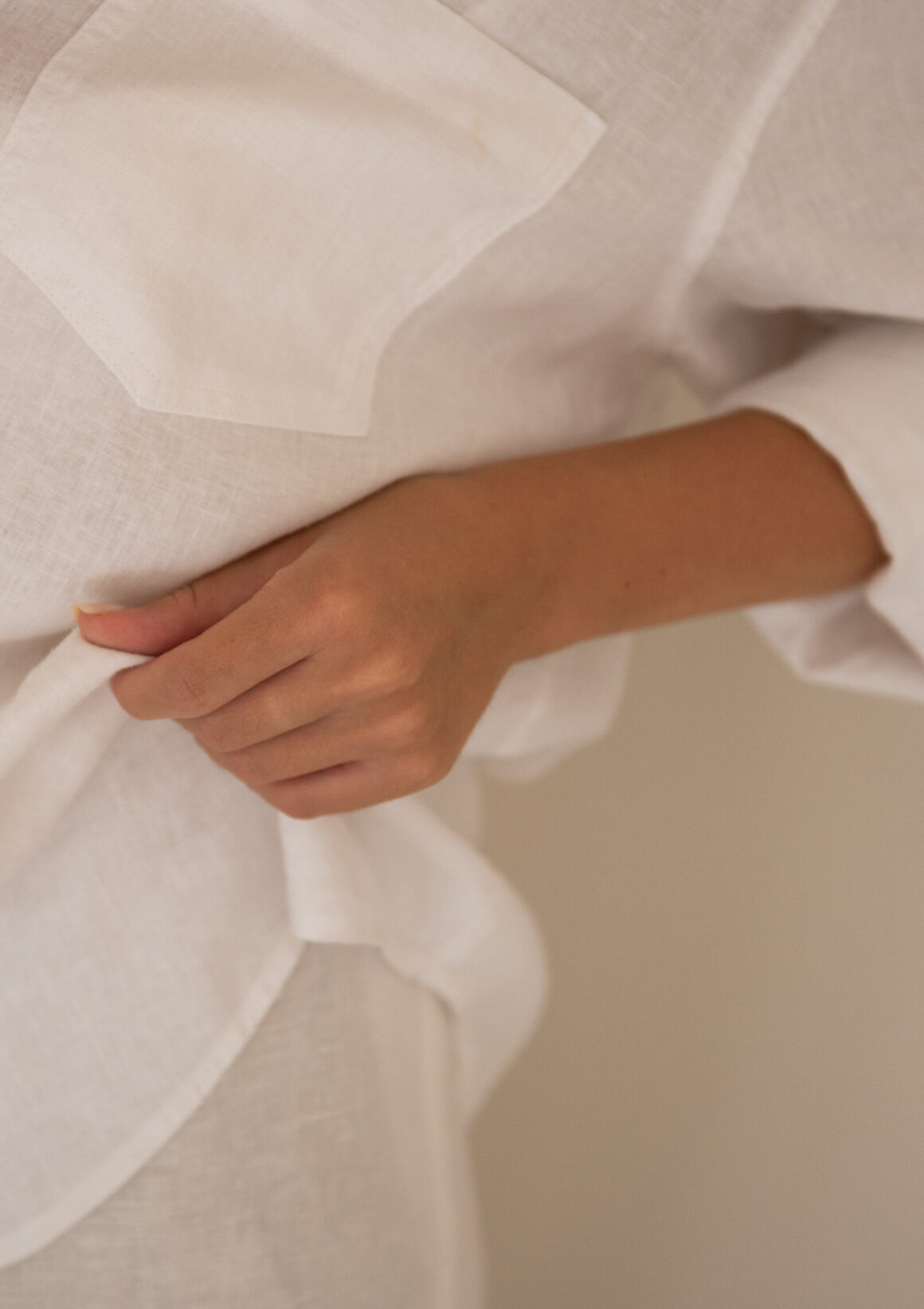 A hand holding the fabric of a loose white linen shirt in soft natural light