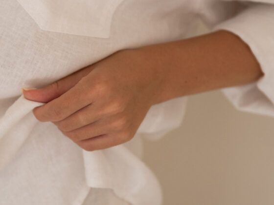 A hand holding the fabric of a loose white linen shirt in soft natural light
