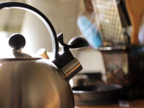 A stainless steel kettle steaming on a stovetop in a sunlit kitchen