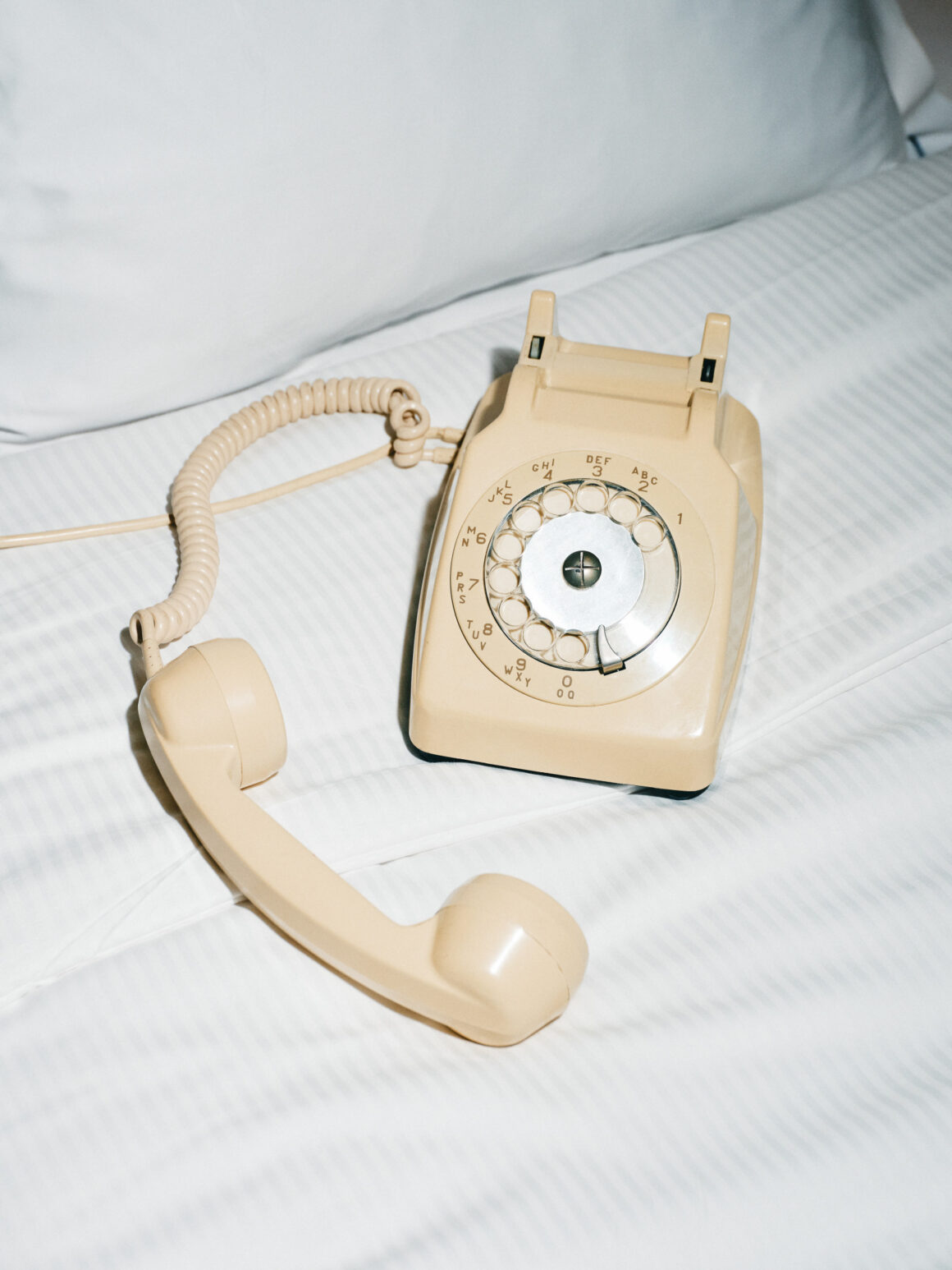 A cream rotary telephone lying off the hook on white bed linens