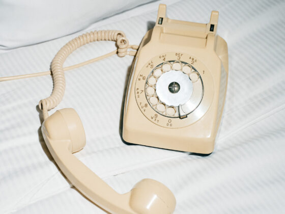 A cream rotary telephone lying off the hook on white bed linens