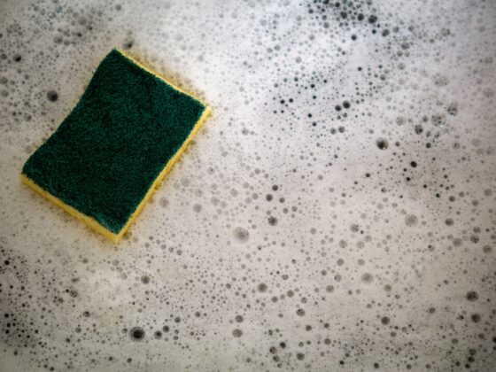 Green and yellow scrub sponge resting in soapy water on a gray surface.