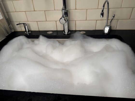 A kitchen sink mounded with dish soap suds