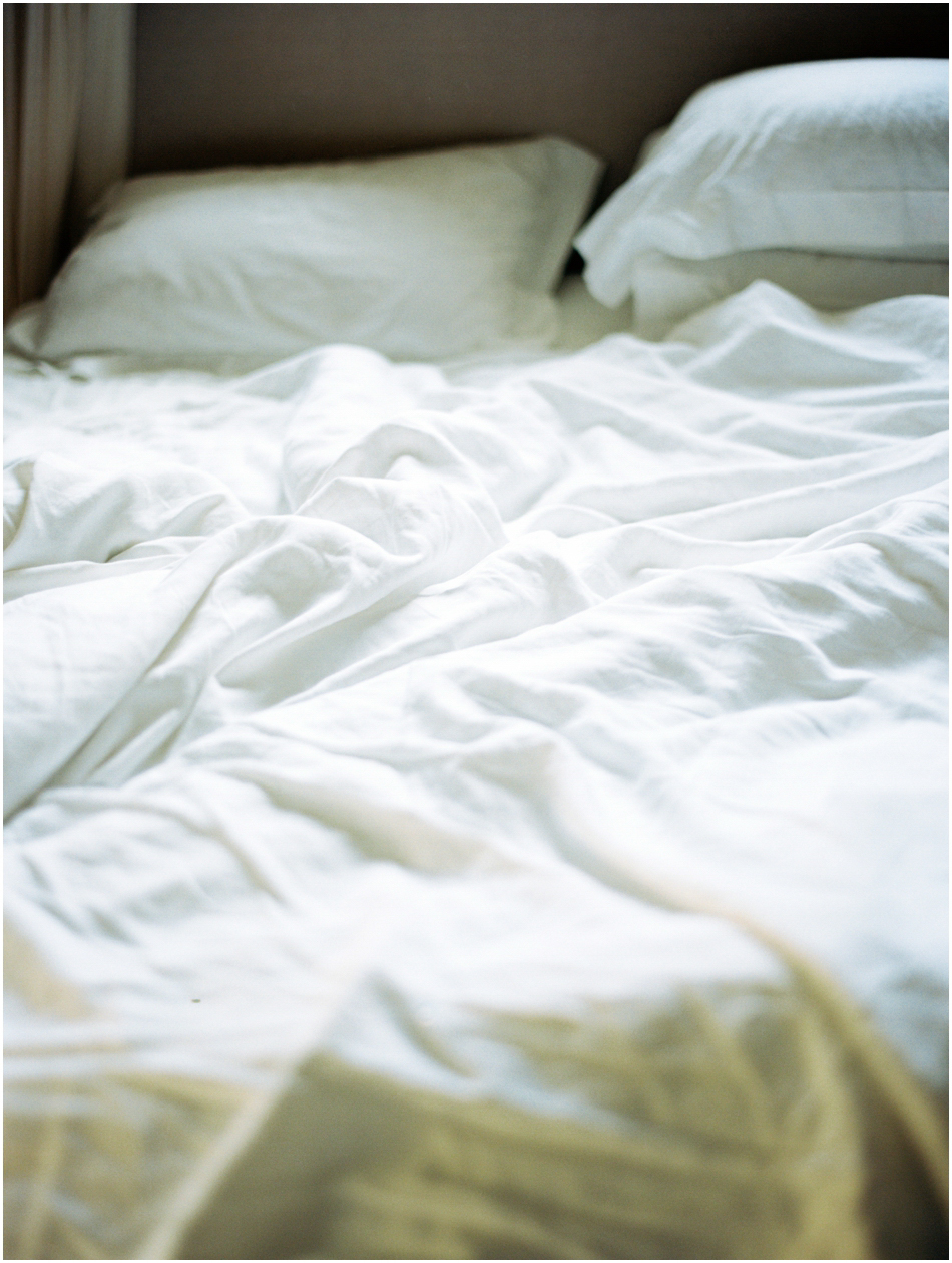 An unmade bed with rumpled white sheets.
