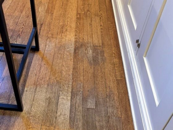 Hardwood floor showing wear in a home where the finish has worn through in a frequently used spot beside a cabinet.