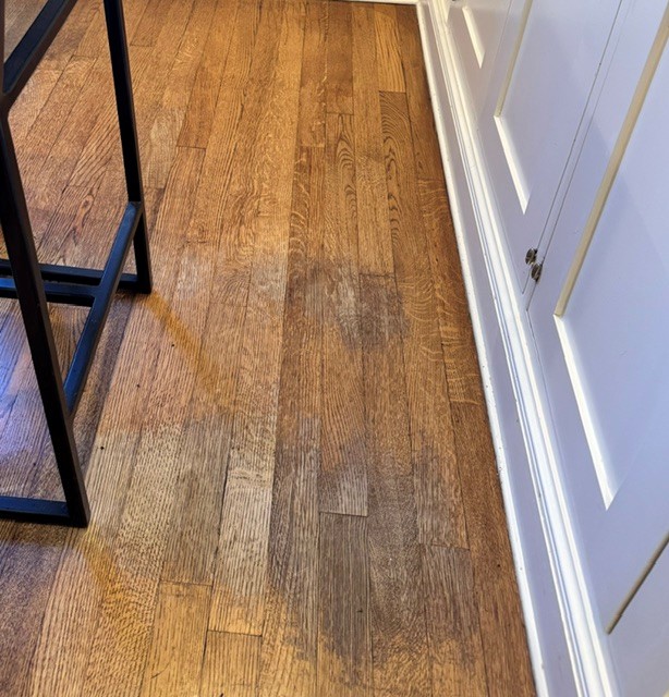 Hardwood floor showing wear in a home where the finish has worn through in a frequently used spot beside a cabinet.