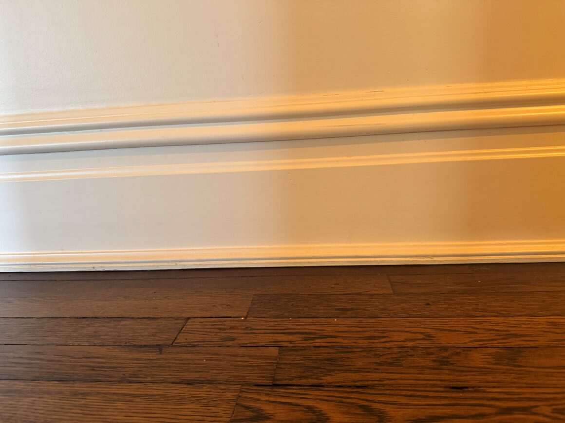 A white painted baseboard where it meets a dark wood floor