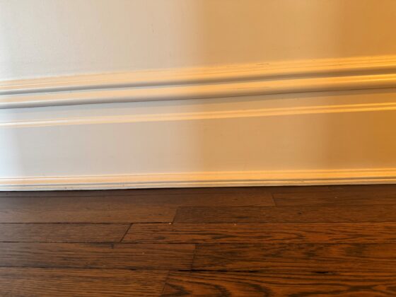 A white painted baseboard where it meets a dark wood floor