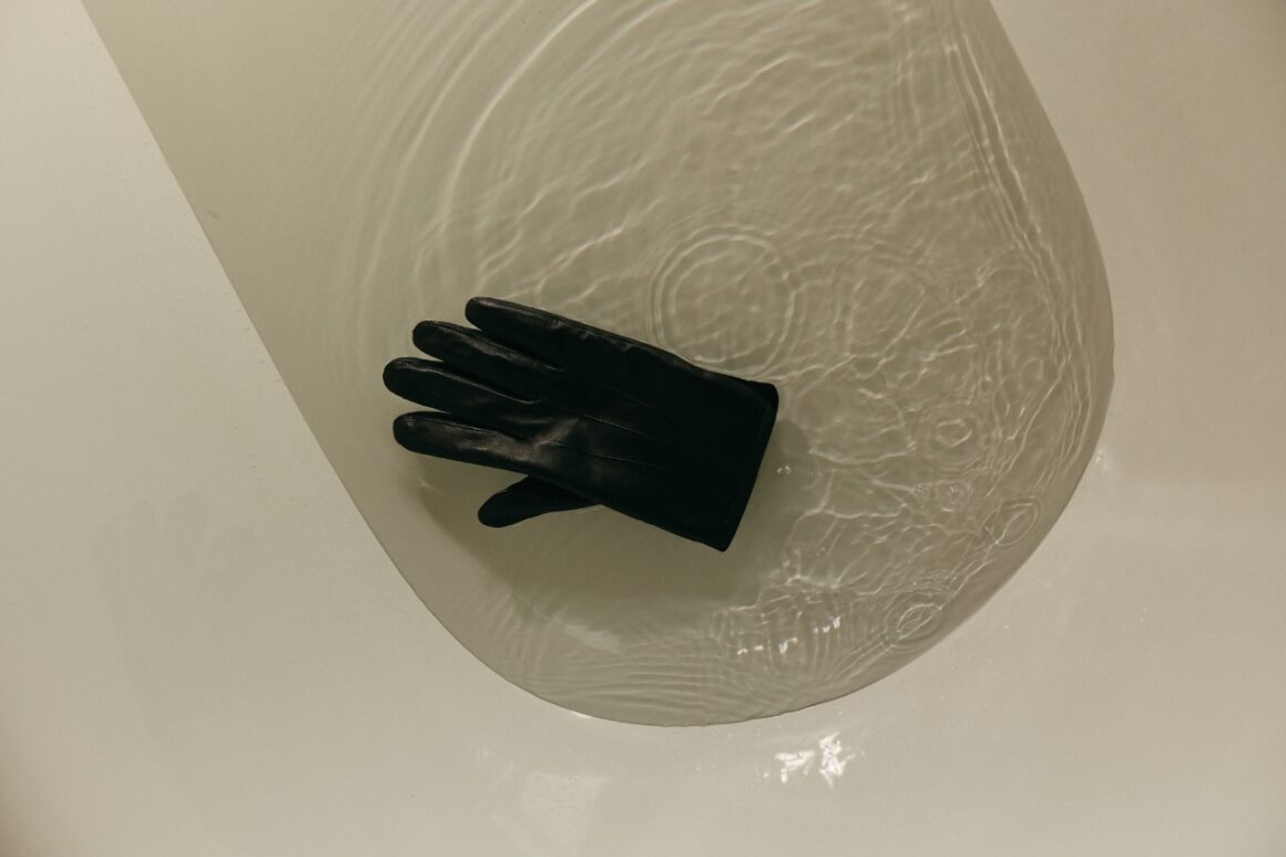 Black glove floating in a bathtub of clear water, seen from above