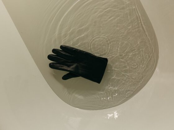 Black glove floating in a bathtub of clear water, seen from above