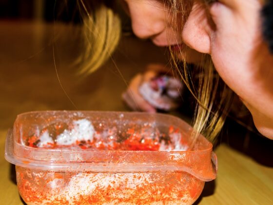 Two children lean over a small plastic container, watching a baking soda and vinegar reaction