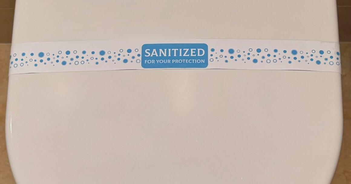 A sanitary band reading "Sanitized for your protection" across a closed white toilet lid