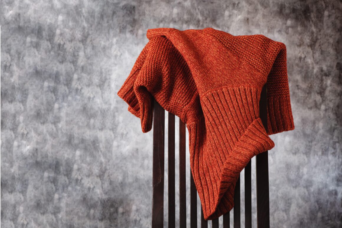 A rust-colored sweater draped over the back of a wooden dining chair.