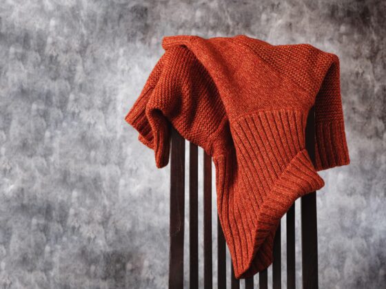 A rust-colored sweater draped over the back of a wooden dining chair.
