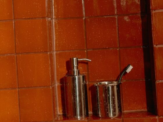 Glossy terracotta shower tile with water droplets and a chrome soap dispenser in a tiled niche